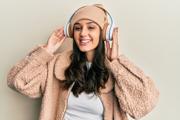 Young hispanic woman listening to music using headphones smiling with a happy and cool smile on face. showing teeth.