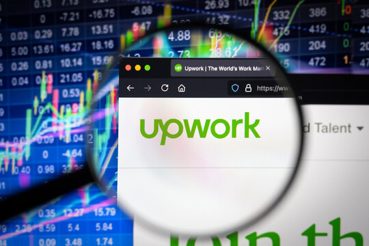 Upwork company logo on a website with blurry stock market developments in the background, seen on a computer screen through a magnifying glass