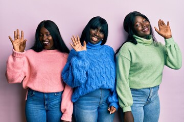 Three young african american friends wearing wool winter sweater waiving saying hello happy and smiling, friendly welcome gesture