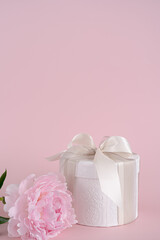 Gift box with ribbon and beautiful pion flower on light pink background.Space for text.Happy birthday, valentine's day, weddings card concept.