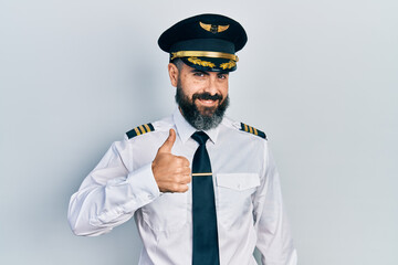 Young hispanic man wearing airplane pilot uniform doing happy thumbs up gesture with hand....