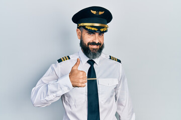 Young hispanic man wearing airplane pilot uniform doing happy thumbs up gesture with hand. approving expression looking at the camera showing success. © Krakenimages.com