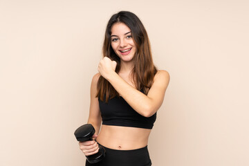 Young sport woman making weightlifting isolated on beige background celebrating a victory