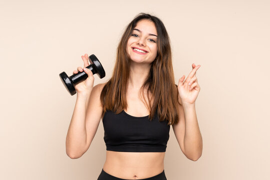 Young sport woman making weightlifting isolated on beige background with fingers crossing © luismolinero