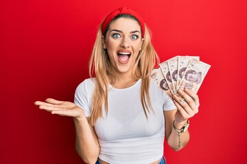 Young caucasian woman holding 500 mexican pesos banknotes celebrating achievement with happy smile...