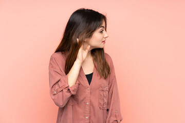 Young caucasian woman isolated on pink background listening to something by putting hand on the ear