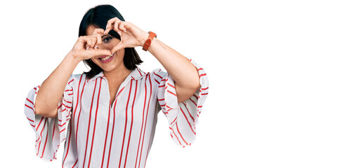 Young hispanic girl wearing casual clothes doing heart shape with hand and fingers smiling looking through sign