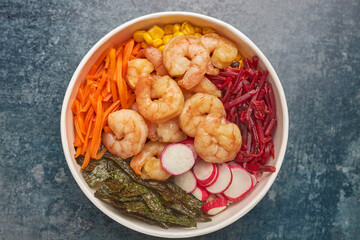 Top view of a shrimp poke with carrots, beets and seaweed.