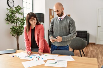 Two hispanic business workers with serious expression working using smartphone at the office.