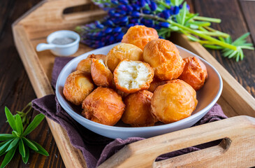 Round fried donuts in a ceramic bowl on a brown wooden background.