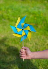 A boy plays with a yellow and blue paper 8-petal weather vane in the garden. Children's creativity,...