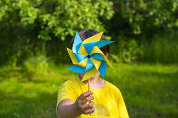 A boy in a yellow jersey plays with a yellow and blue paper 8-petal weather vane in the garden....