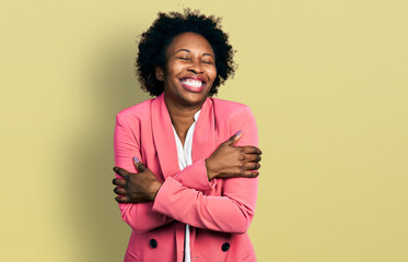African american woman with afro hair wearing business jacket hugging oneself happy and positive, smiling confident. self love and self care