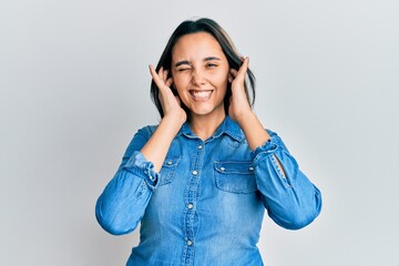 Young hispanic woman wearing casual denim jacket covering ears with fingers with annoyed expression for the noise of loud music. deaf concept.