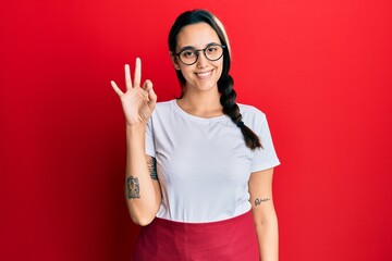 Young hispanic woman wearing professional waitress apron smiling positive doing ok sign with hand and fingers. successful expression.