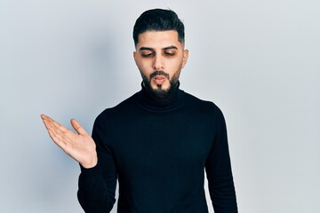 Handsome man with beard presenting with open palm making fish face with mouth and squinting eyes, crazy and comical.