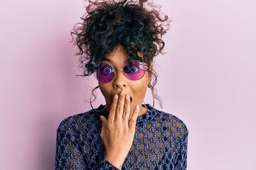 Young hispanic woman wearing cool sunglasses covering mouth with hand, shocked and afraid for...