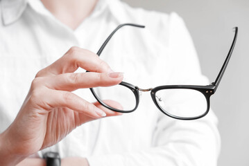 Woman holding optical glasses in a black frame on a white background. Copy, empty space