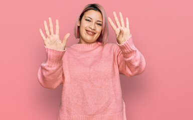Hispanic woman with pink hair wearing casual winter sweater showing and pointing up with fingers...
