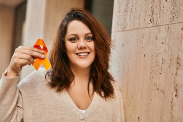 Young irish plus size girl smiling happy holding orange awareness ribbon at the city.