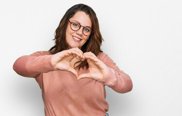Fototapeta premium Young plus size woman wearing casual clothes and glasses smiling in love doing heart symbol shape with hands. romantic concept.
