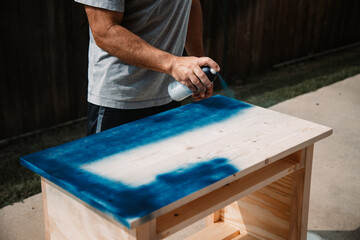 Man painting a wooden table in broad strokes with blue spray paint