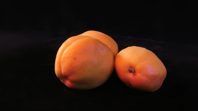 There are three ripe golden-colored fruits on a dark background. A rotating video.