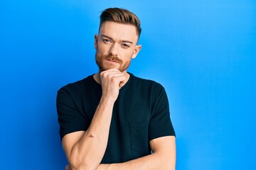 Young redhead man wearing casual black t shirt thinking concentrated about doubt with finger on...