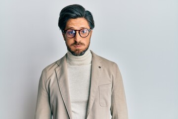 Young hispanic man wearing business jacket and glasses puffing cheeks with funny face. mouth...