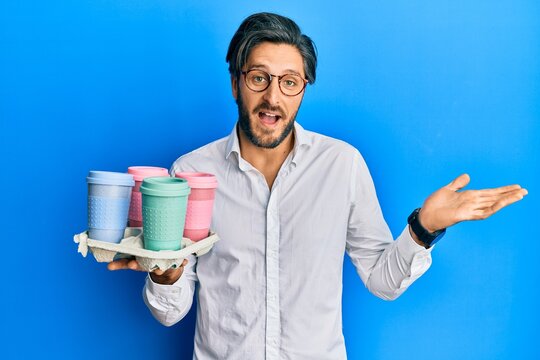 Young hispanic man holding tray with take away coffee celebrating achievement with happy smile and winner expression with raised hand