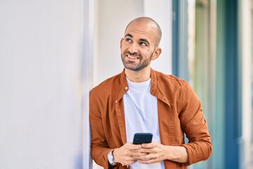 Young hispanic bald man smiling happy using smartphone at the city.