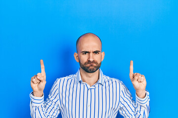 Young bald man pointing up with fingers skeptic and nervous, frowning upset because of problem. negative person.
