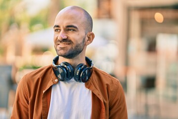 Obraz premium Young hispanic bald man smiling happy using headphones at the city