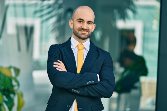 Young hispanic bald businessman with arms crossed smiling happy at the city.