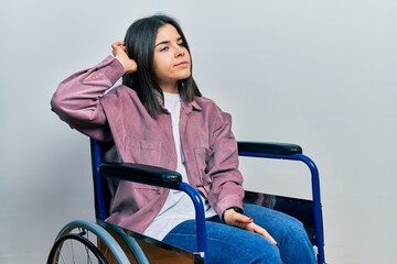 Young brunette woman sitting on wheelchair confuse and wondering about question. uncertain with...