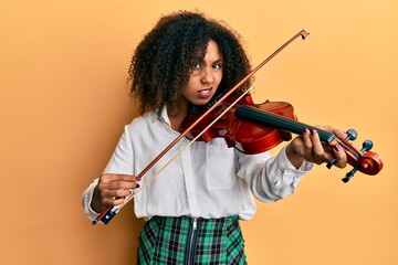 Beautiful african american woman with afro hair playing classical violin clueless and confused...