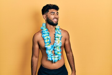Arab man with beard wearing swimsuit and hawaiian lei looking away to side with smile on face,...