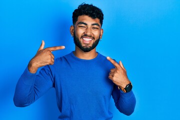 Arab man with beard wearing casual blue sweater smiling cheerful showing and pointing with fingers teeth and mouth. dental health concept.