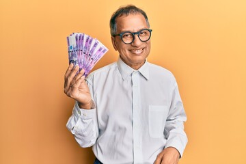 Middle age indian man holding 100 philippine peso banknotes looking positive and happy standing and smiling with a confident smile showing teeth