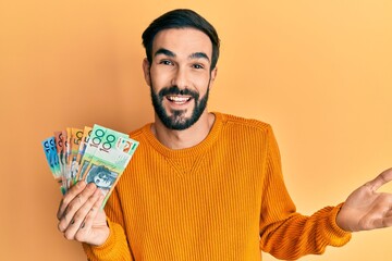 Young hispanic man holding australian dollars celebrating achievement with happy smile and winner expression with raised hand