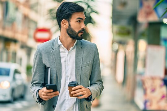 Young hispanic businessman with serious expression using smartphone and drinking coffee at the city.