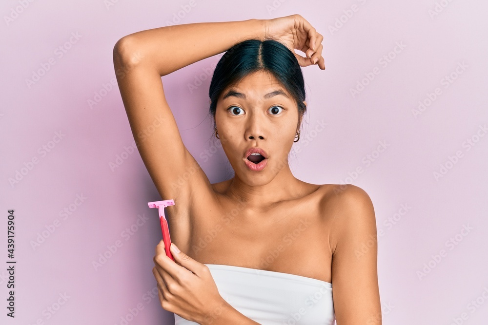 Sticker young chinese woman wearing shower towel using razor afraid and shocked with surprise and amazed exp