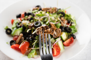 Escargot grape snail on fork near green salad on white background. French gourmet cuisine.
