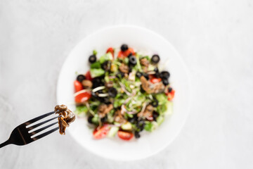Escargot grape snail on fork near green salad on white background. French gourmet cuisine.