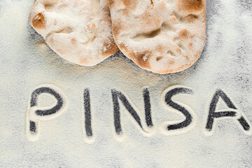Dough and flour with text pinsa on black background. Pinsa romana and scrocchiarella gourmet italian cuisine. Traditional dish in italy.