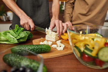 Man cutting cheese for salad while cooking