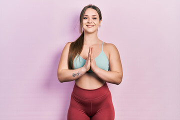 Young hispanic girl wearing sportswear praying with hands together asking for forgiveness smiling confident.