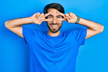 Naklejka premium Young hispanic man wearing casual clothes doing peace symbol with fingers over face, smiling cheerful showing victory