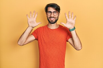 Young hispanic man wearing casual clothes and glasses showing and pointing up with fingers number ten while smiling confident and happy.