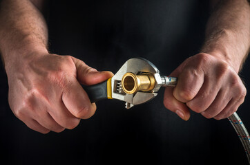 The plumber connects the hose and brass fitting using an adjustable wrench. The work combines...
